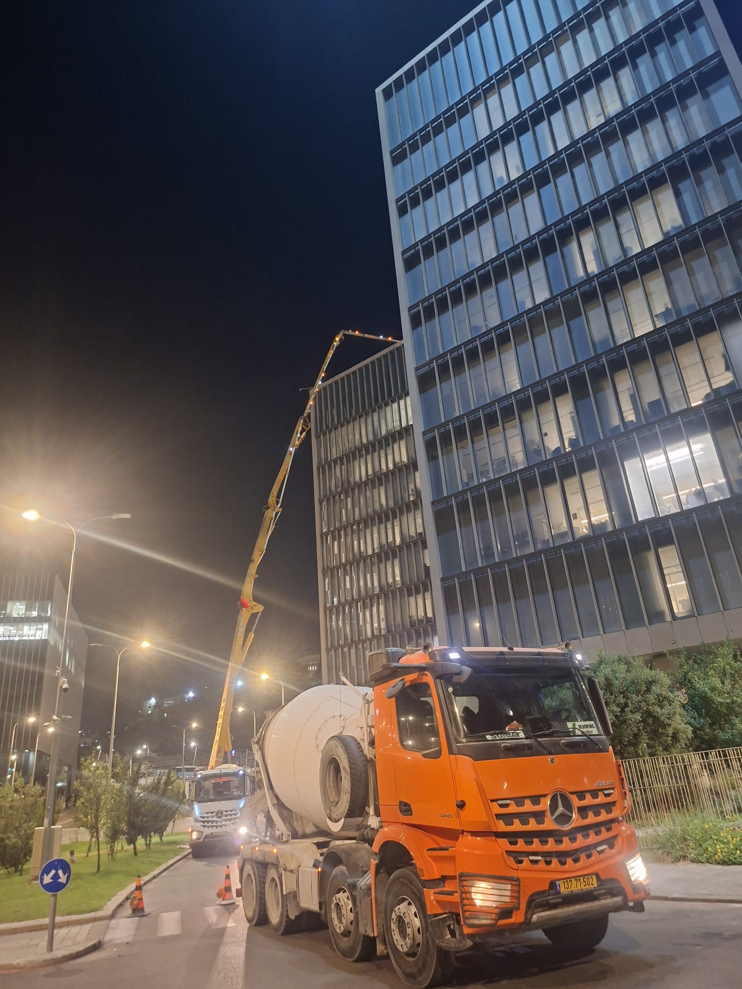 יציקת בטון לילית עם משאבת בטון ליד בניין משרדים