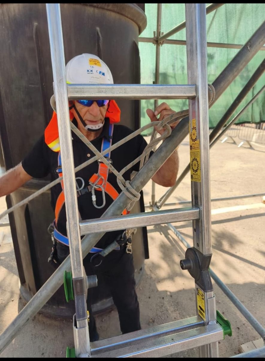 עלייה מאובטחת על סולם עם רתמת בטיחות וקסדה באתר